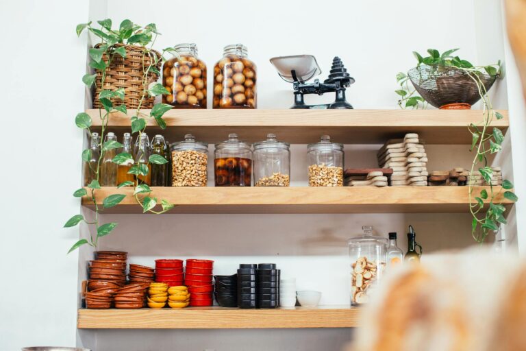 Timber shelves with many glass jars filled with nuts near green potted plants and plastic containers